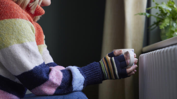 woman holding a warm mug by a radiator